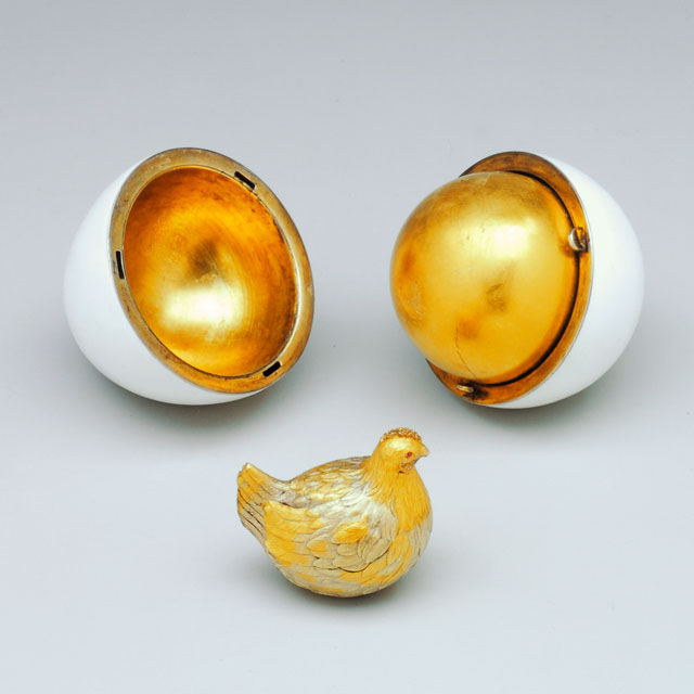 An egg split apart with a golden inside and a small golden hen in front of it.