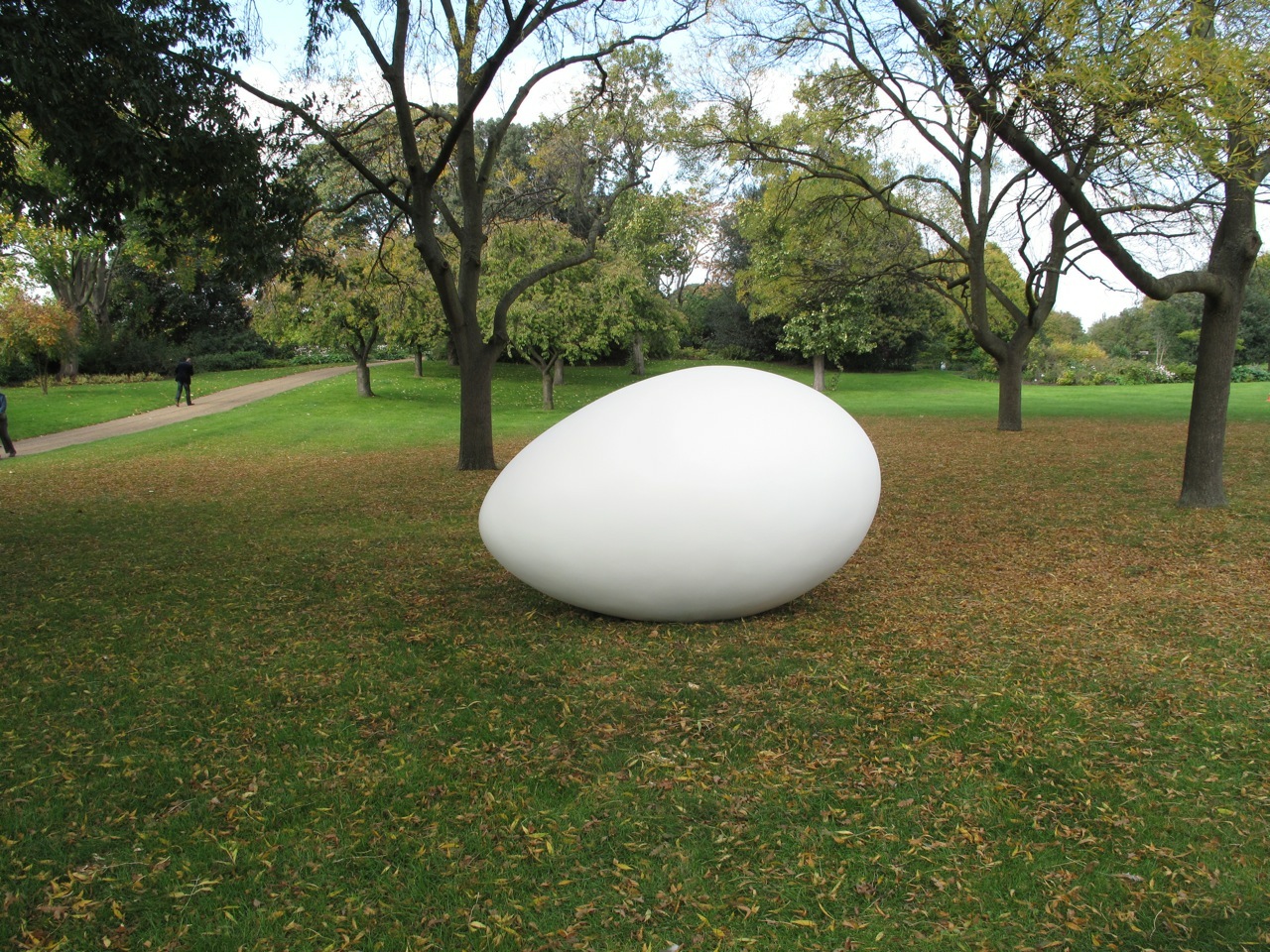 A large egg sculpture sits on a field in what looks like a public park