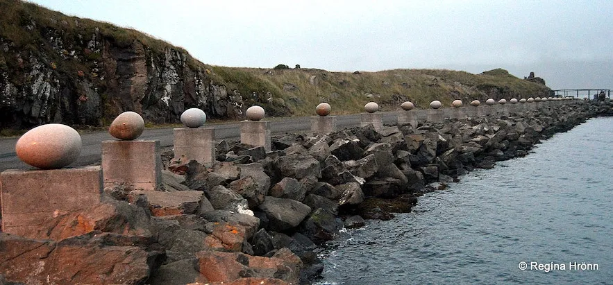 A wide shot of 34 large granite eggs set on plinths lining a road on one side and the ocean on the other